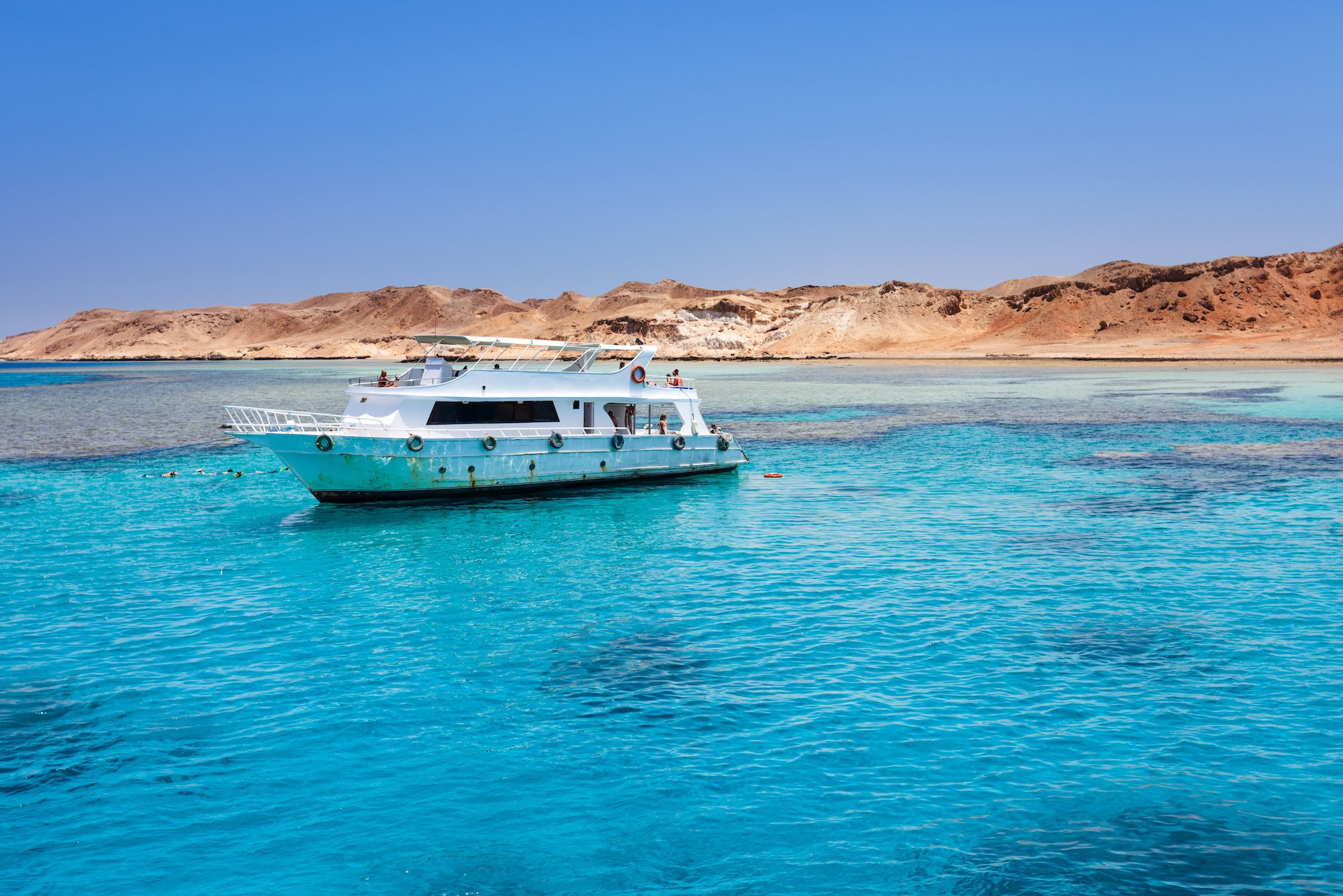 Yacht sailing in open waters with desert mountains in background, Red Sea region