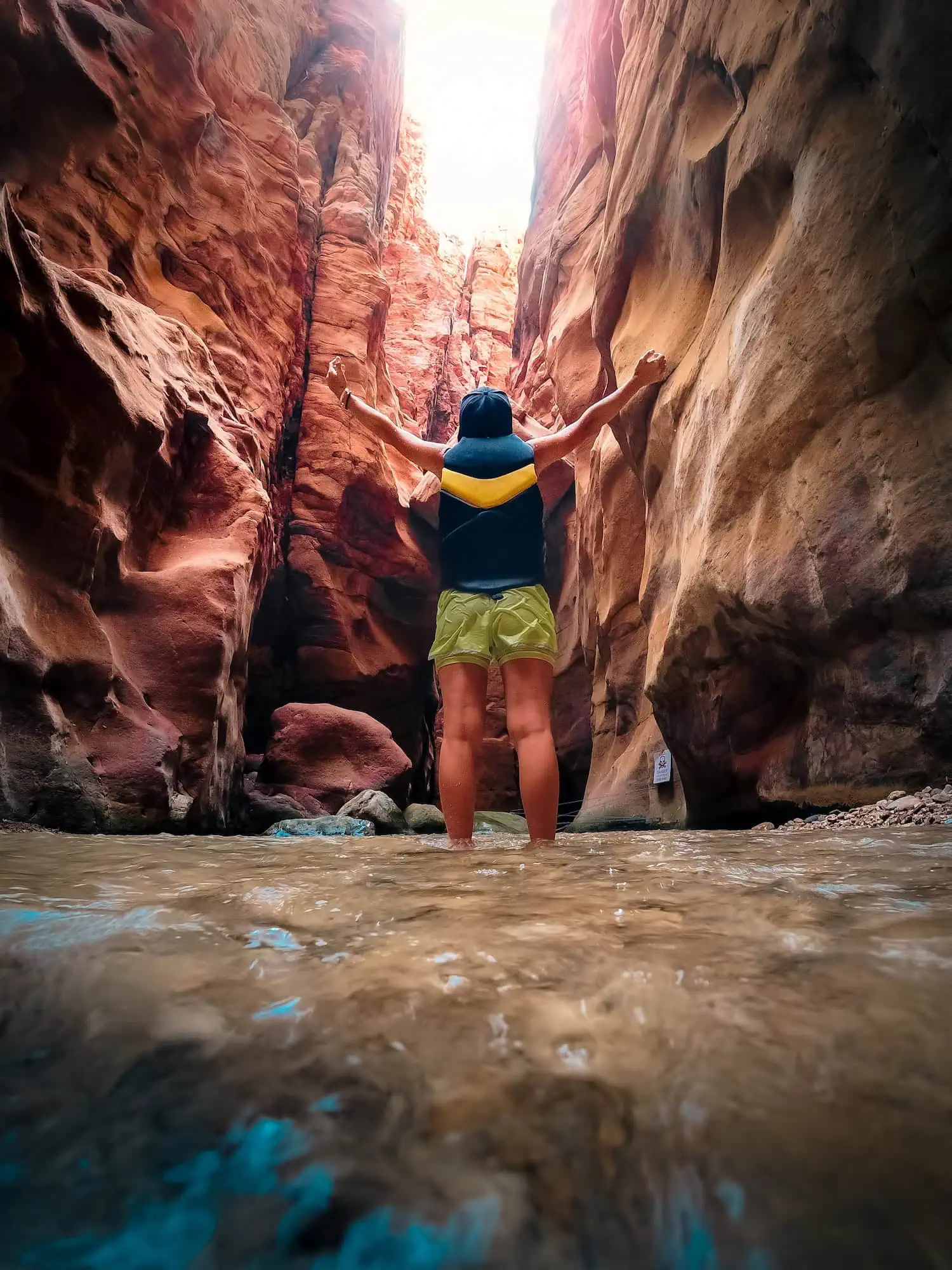 Tourist standing with arms outstretched in narrow Wadi Mujib canyon with red sandstone walls