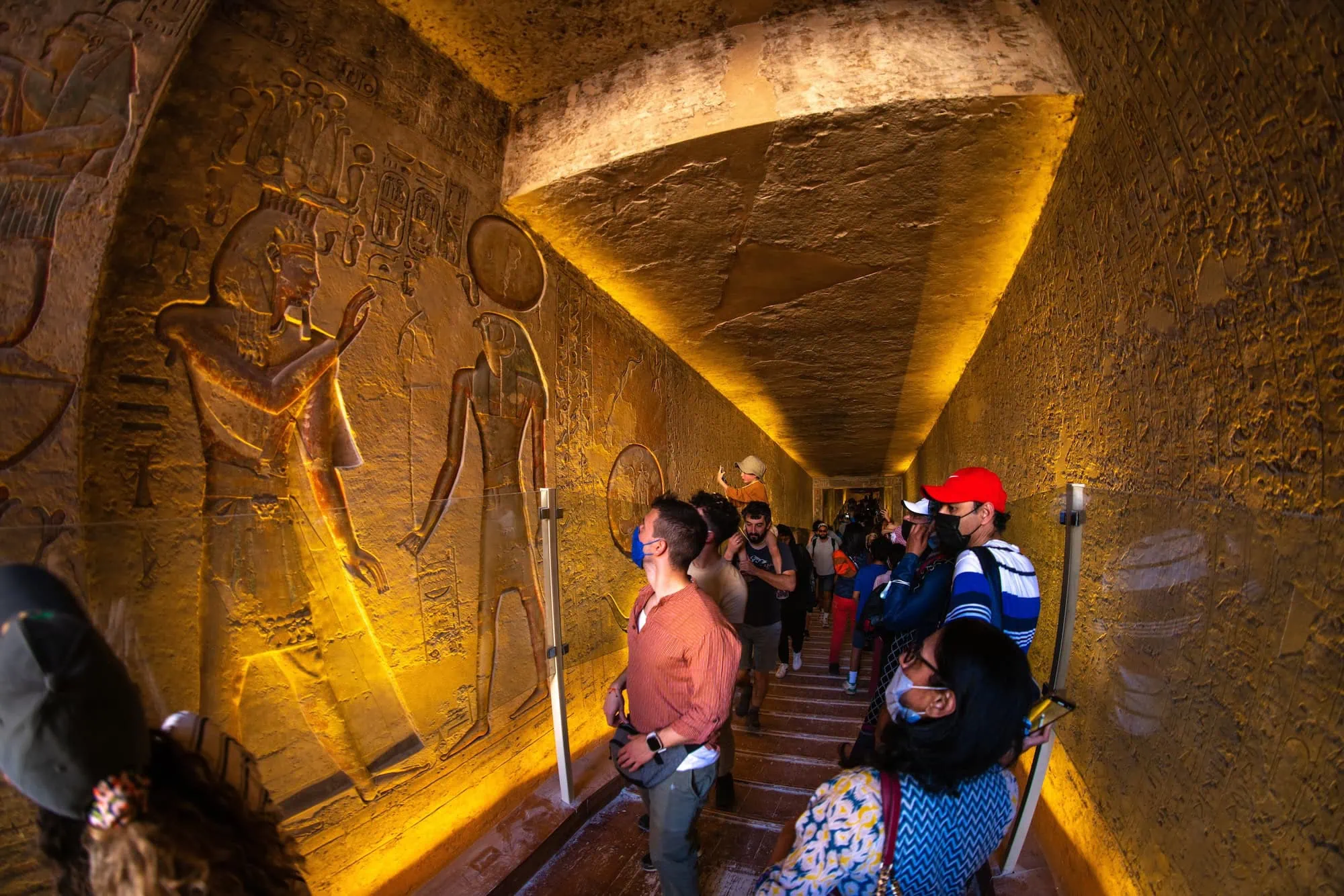 Tourists exploring ancient Egyptian tomb interior with hieroglyphic walls in Valley of the Kings