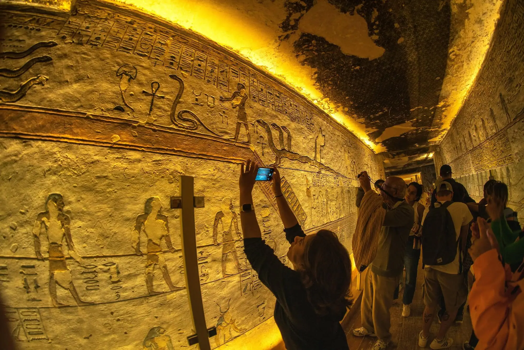 Tourist photographing ancient Egyptian hieroglyphic wall carvings inside temple