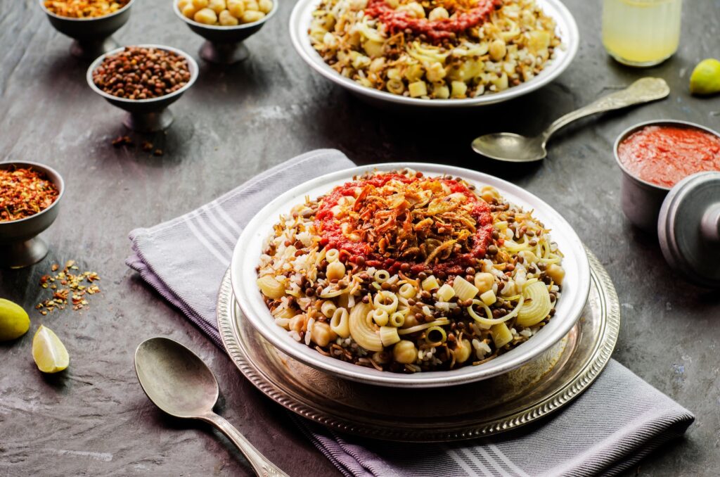 Plate of koshari with rice, pasta, lentils, chickpeas, fried onions, tomato garlic sauce