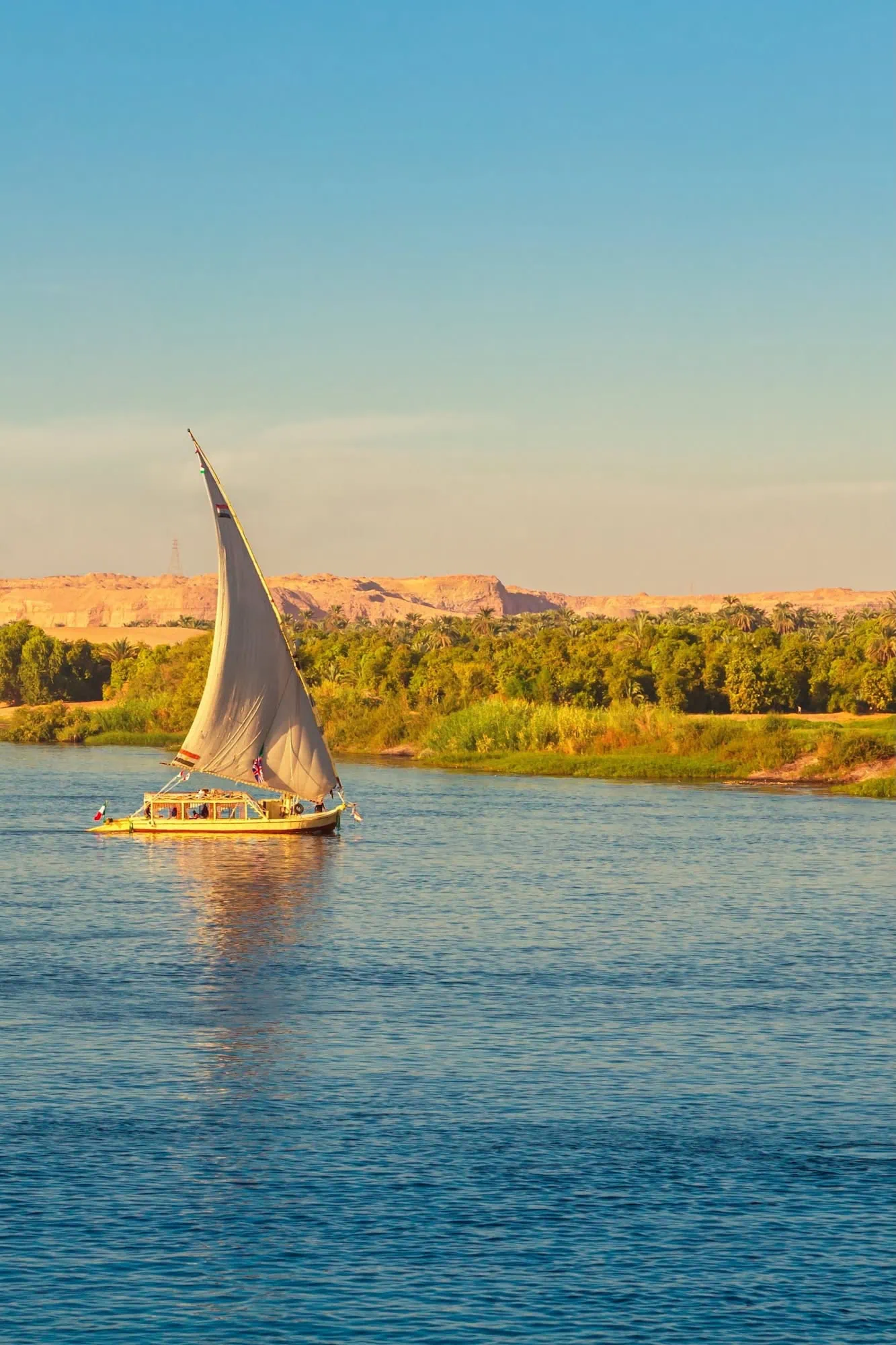 Traditional felucca sailboat sailing on the Nile River at sunset near Aswan