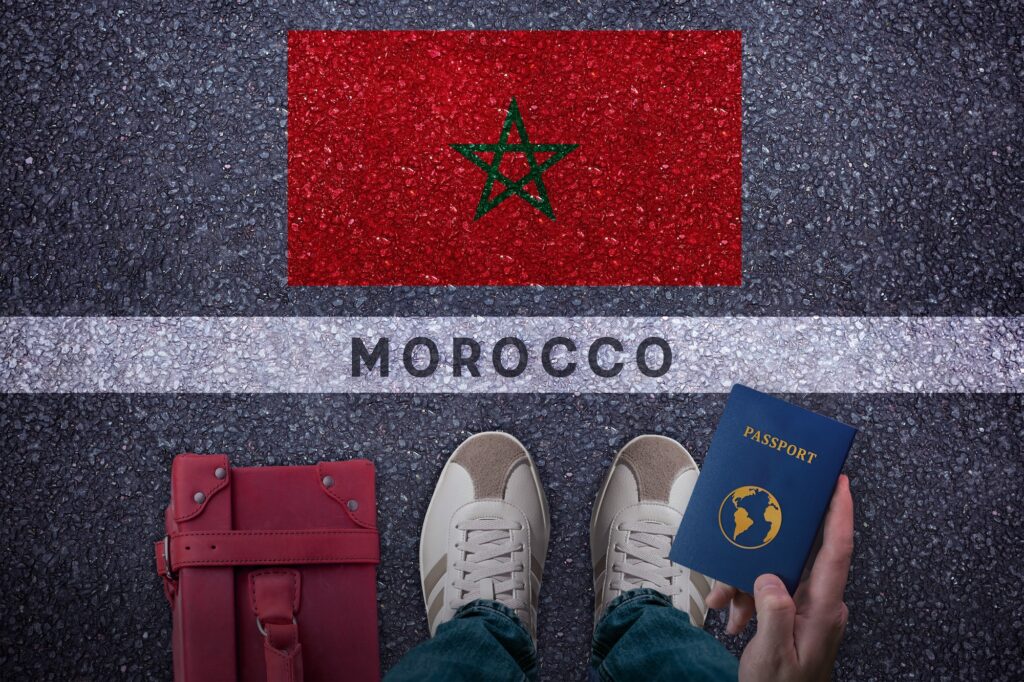 Travel to Morocco. Traveler perspective with bag passport and Morocco flag on asphalt road
