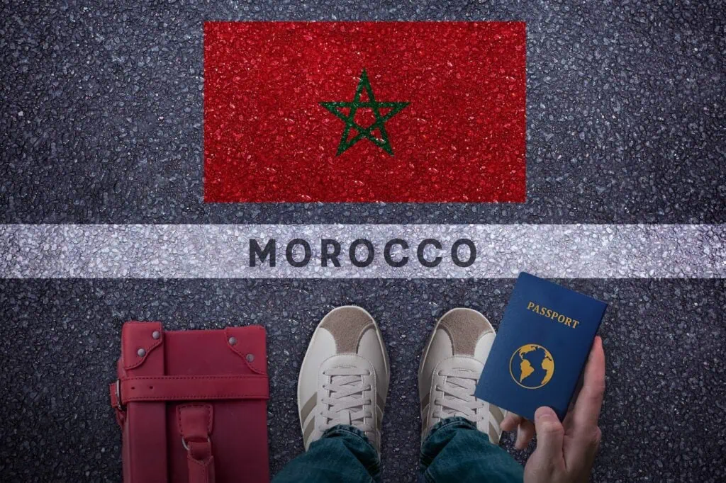 Travel to Morocco. Traveler perspective with bag passport and Morocco flag on asphalt road