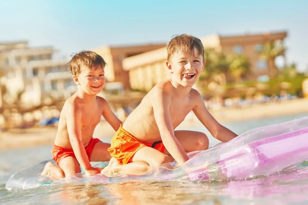 Two boys playing in a hotel swimming pool with resort buildings in the background, Hurghada