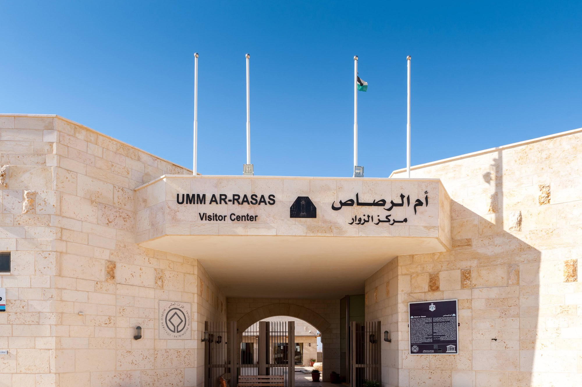 Entrance to Umm ar-Rasas Visitor Center with stone archway and flags