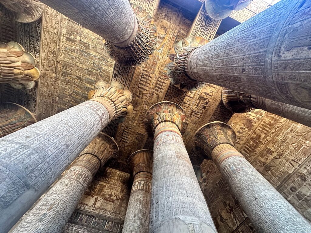 Upward view of painted stone columns and hieroglyph-covered ceiling inside the Temple of Khnum, Esna