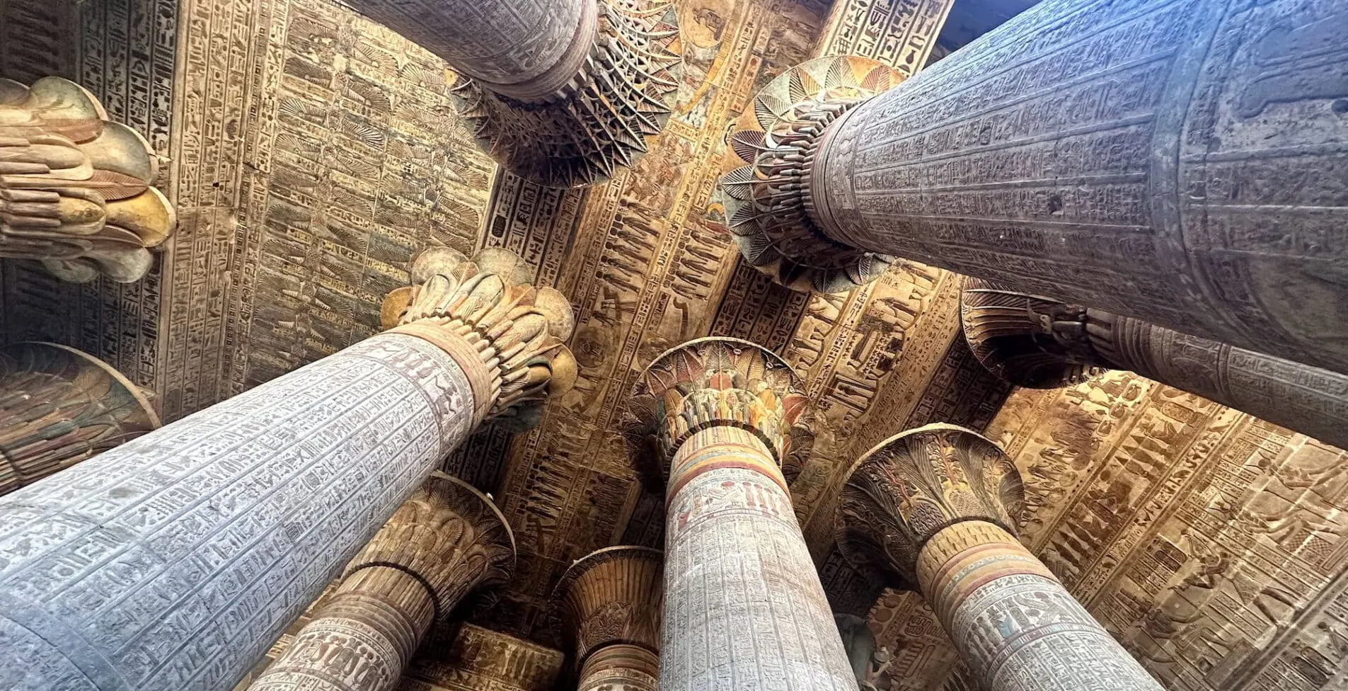 Upward view of painted stone columns and hieroglyph covered ceiling inside the Temple of Khnum Esna 1905x976 crop 53 32