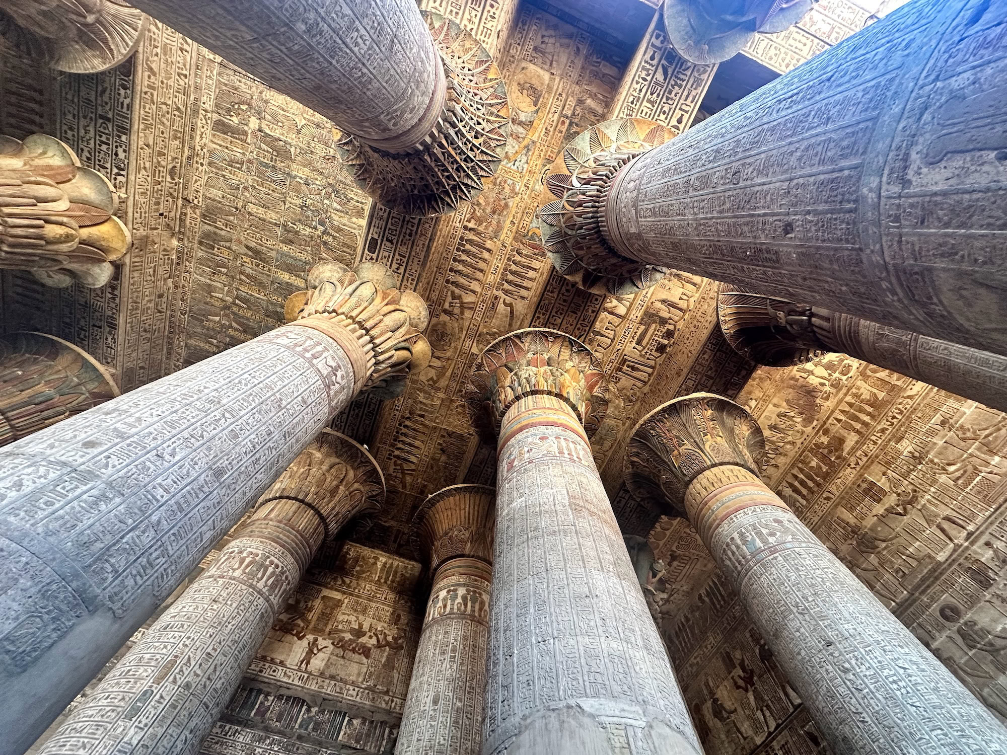 Upward view of painted stone columns and hieroglyph covered ceiling inside the Temple of Khnum Esna