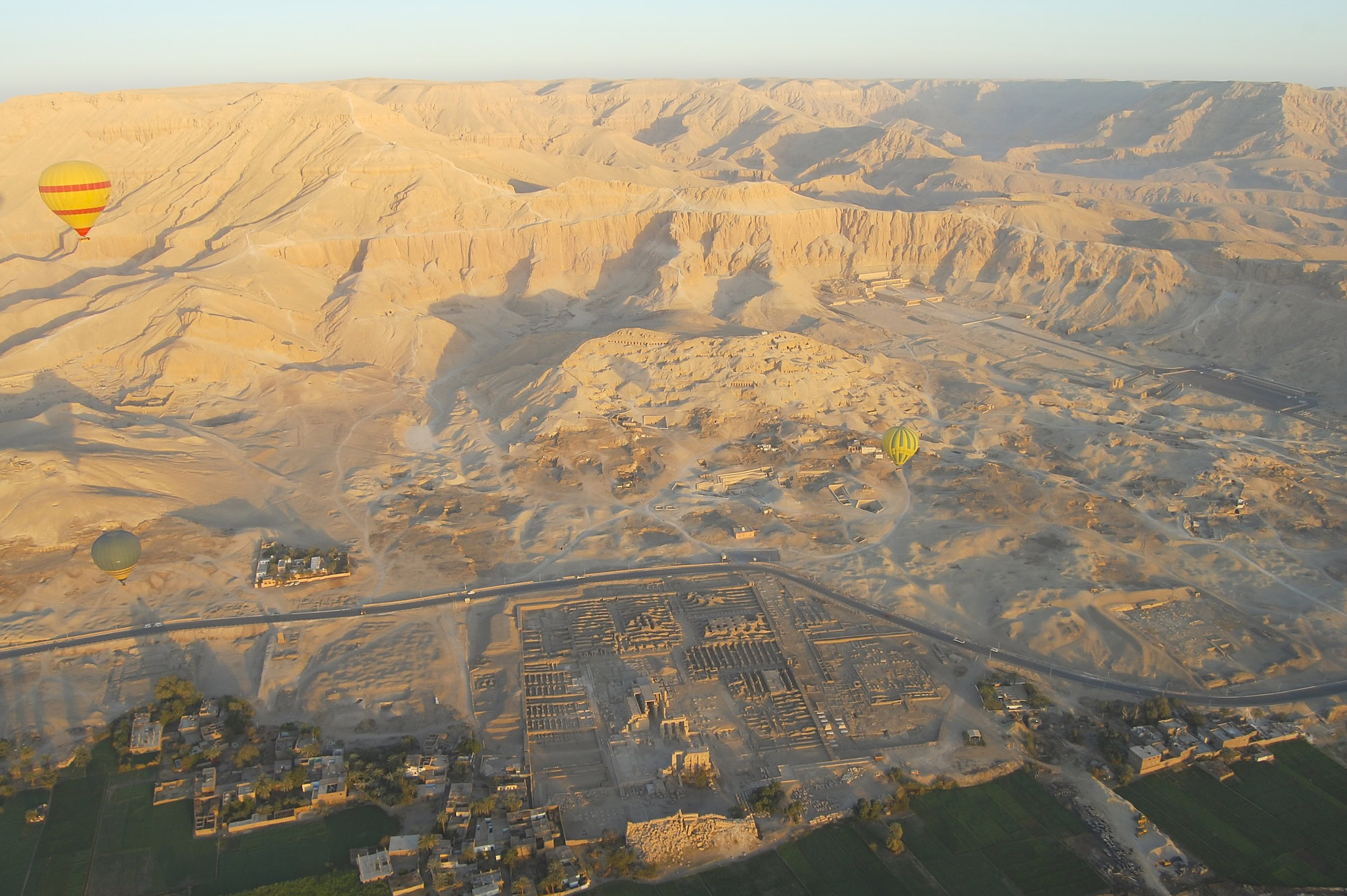 Aerial view of Valley of the Kings archaeological site with hot air balloons and desert mountains
