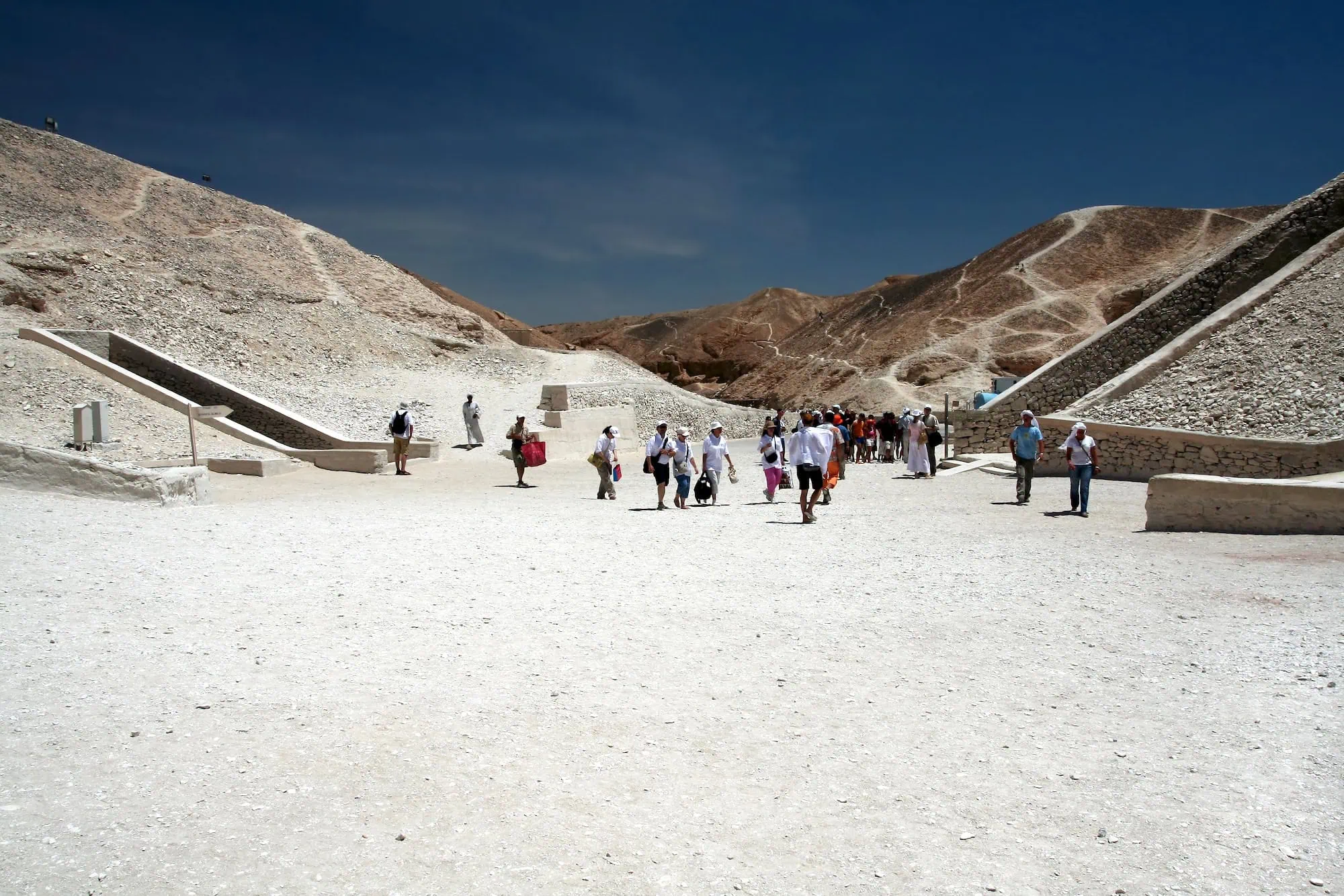Tourists exploring pathways at Valley of the Kings entrance with desert hills and ancient stone structures