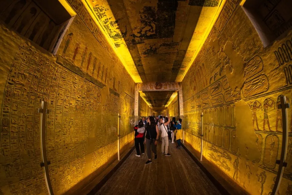 Tourist walking inside a decorated rock-cut tomb corridor with carved walls, Valley of the Kings, Luxor