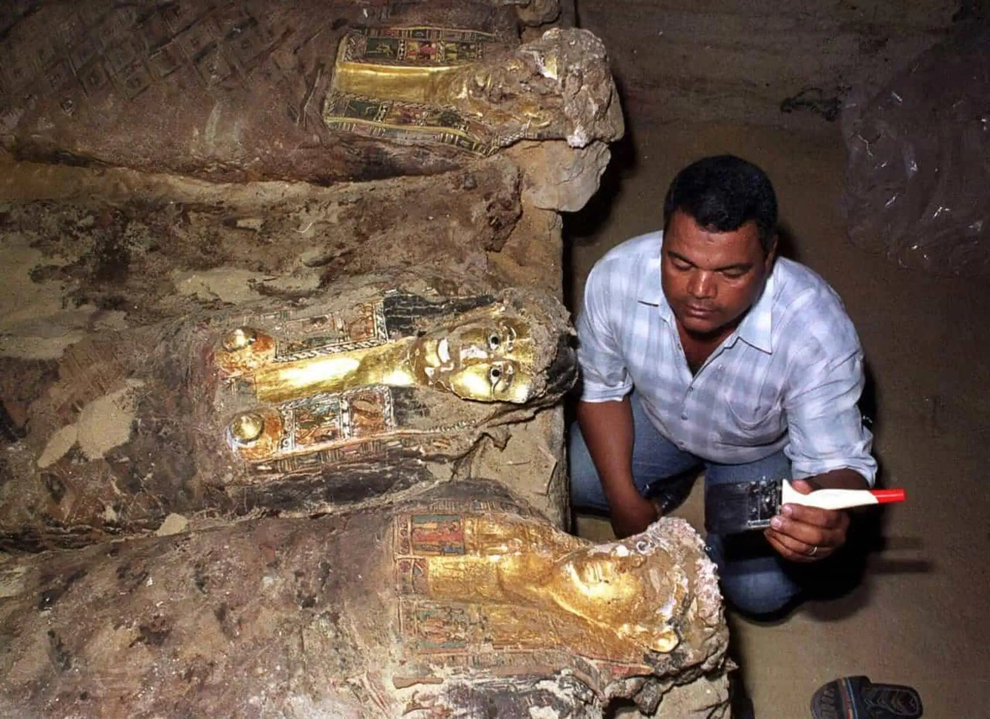 Archaeologist documenting golden mummies at excavation site with preservation equipment