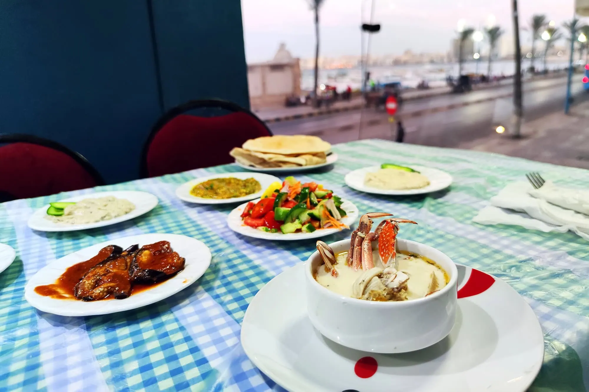 Various seafood dishes served on a restaurant table with night city lights and sea view in the background, Alexandria