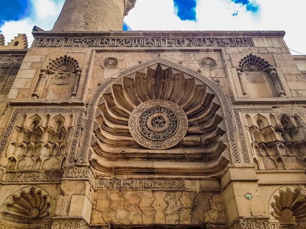 A close-up view of carved stone reliefs and geometric details on the facade of the Al-Aqmar Mosque, Cairo