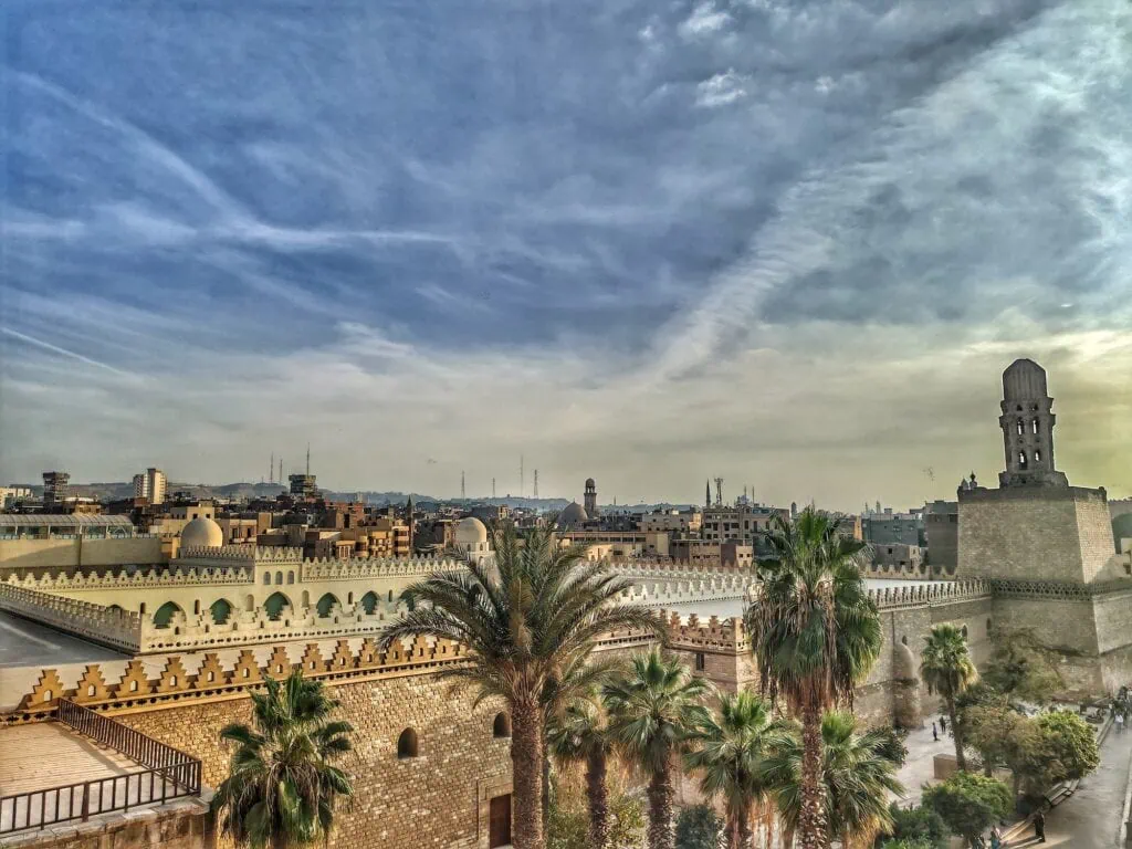A rooftop view overlooking the courtyard, minarets, and stone walls of Al-Hakim Mosque seen from Bab Al-Futuh, Cairo