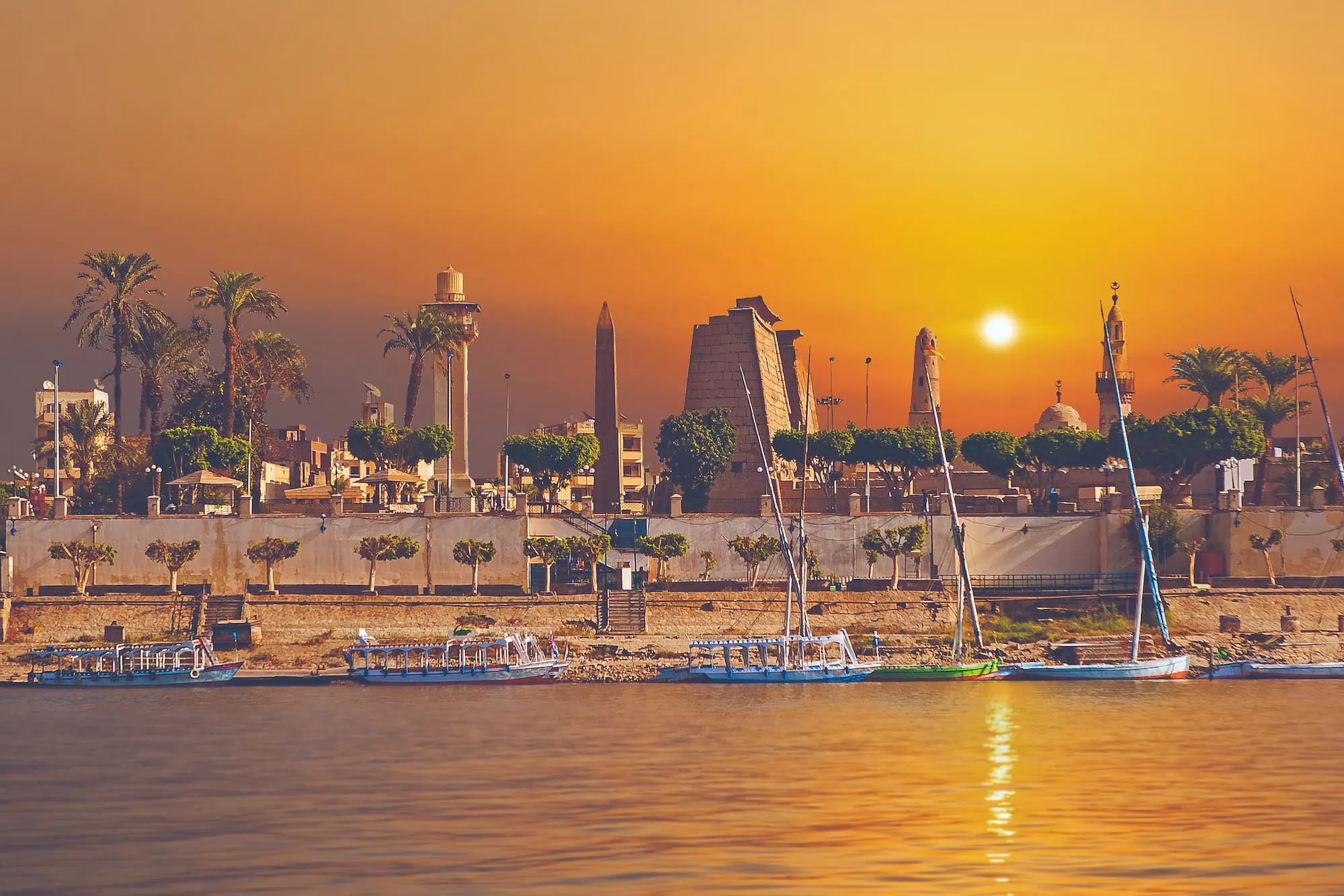 Luxor Temple obelisk overlooking the Nile River with traditional felucca sailboats at sunset