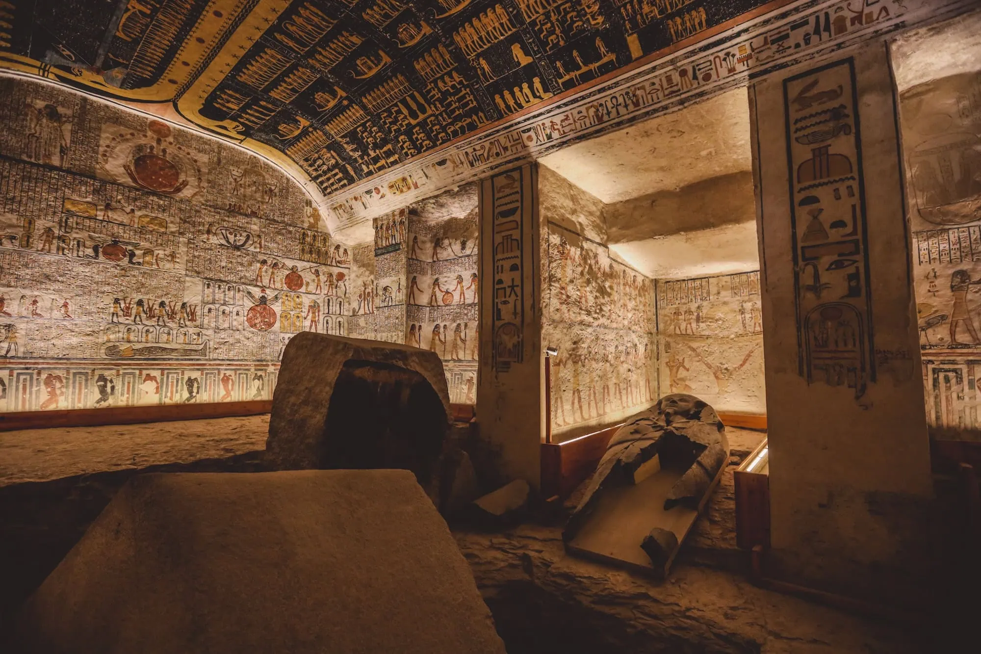 Interior of ancient Egyptian royal tomb chamber showing decorated walls with hieroglyphics and stone sarcophagi in Valley of the Kings