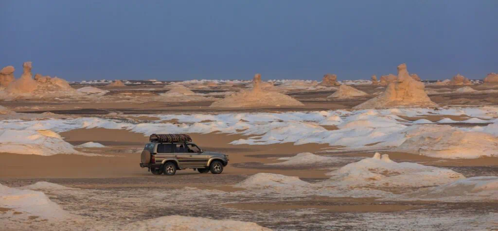 Off-road vehicle driving through White Desert limestone formations near Bahariya Oasis