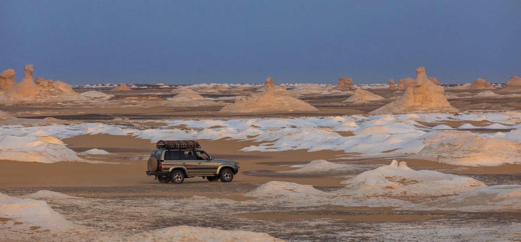 4x4 vehicle traversing White Desert chalk formations at sunset in Egypt