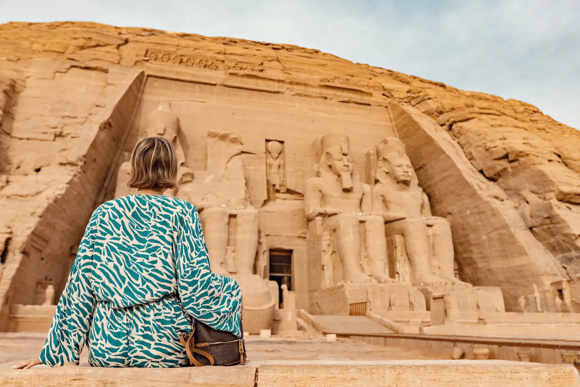 Tourist sitting at Abu Simbel Temple with colossal pharaoh statues in background