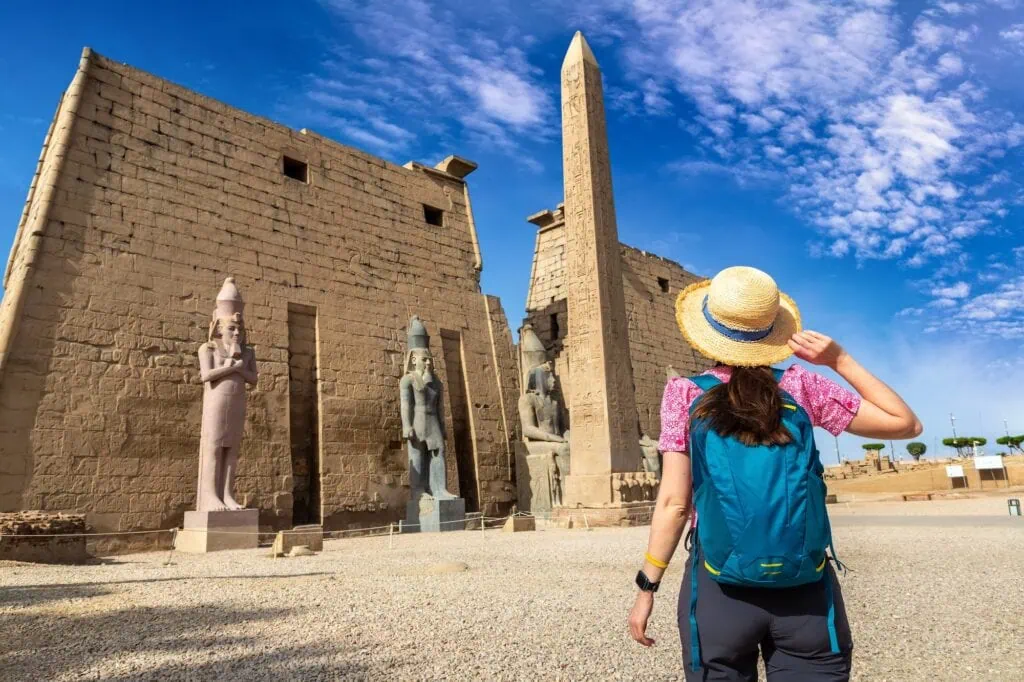 Woman tourist standing near the stone statues and pylons of Luxor Temple on a sunny day, Luxor
