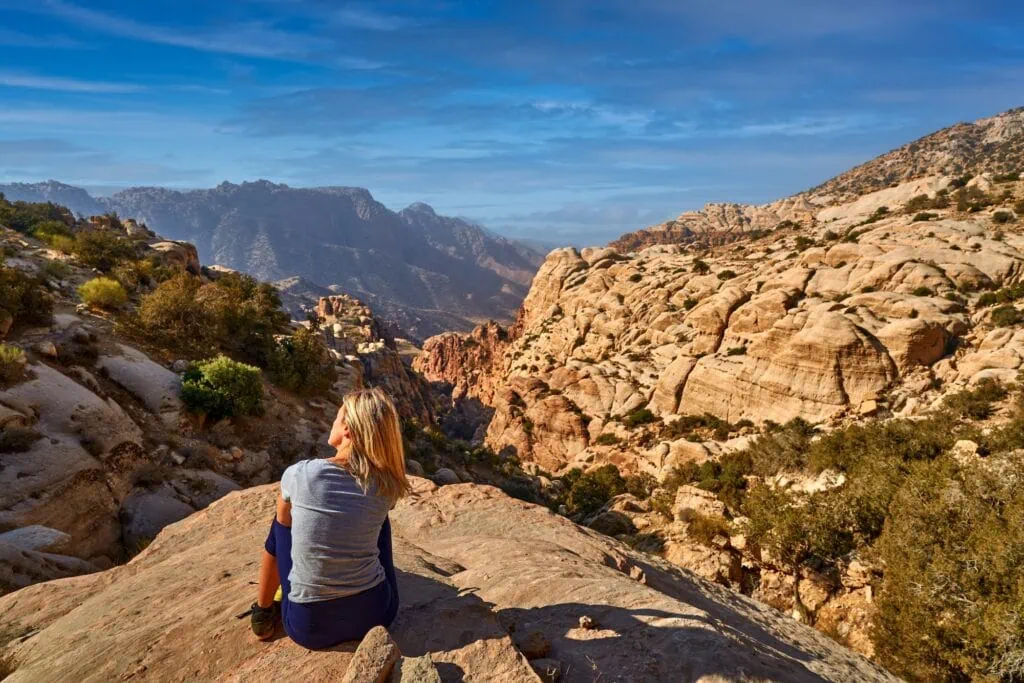 Woman overlooking rocky mountains and sunset valley landscape in Dana Biosphere Reserve Dana
