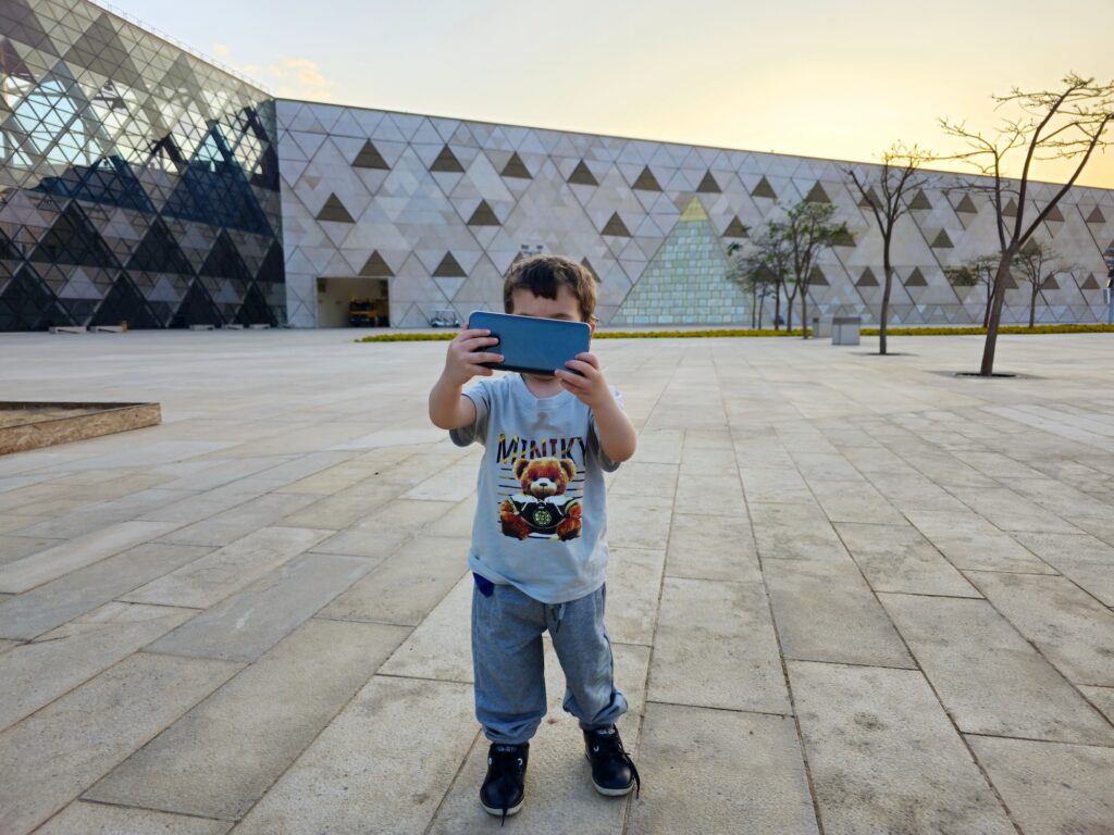 Young tourist child taking a selfie outside the Grand Egyptian Museum entrance, Giza