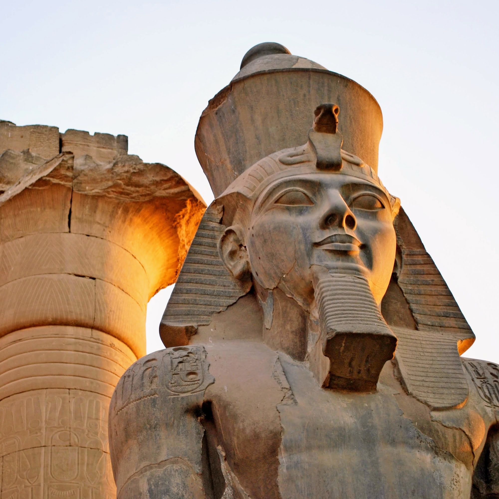 ancient Pharaoh statue and column on backlighted sky background
