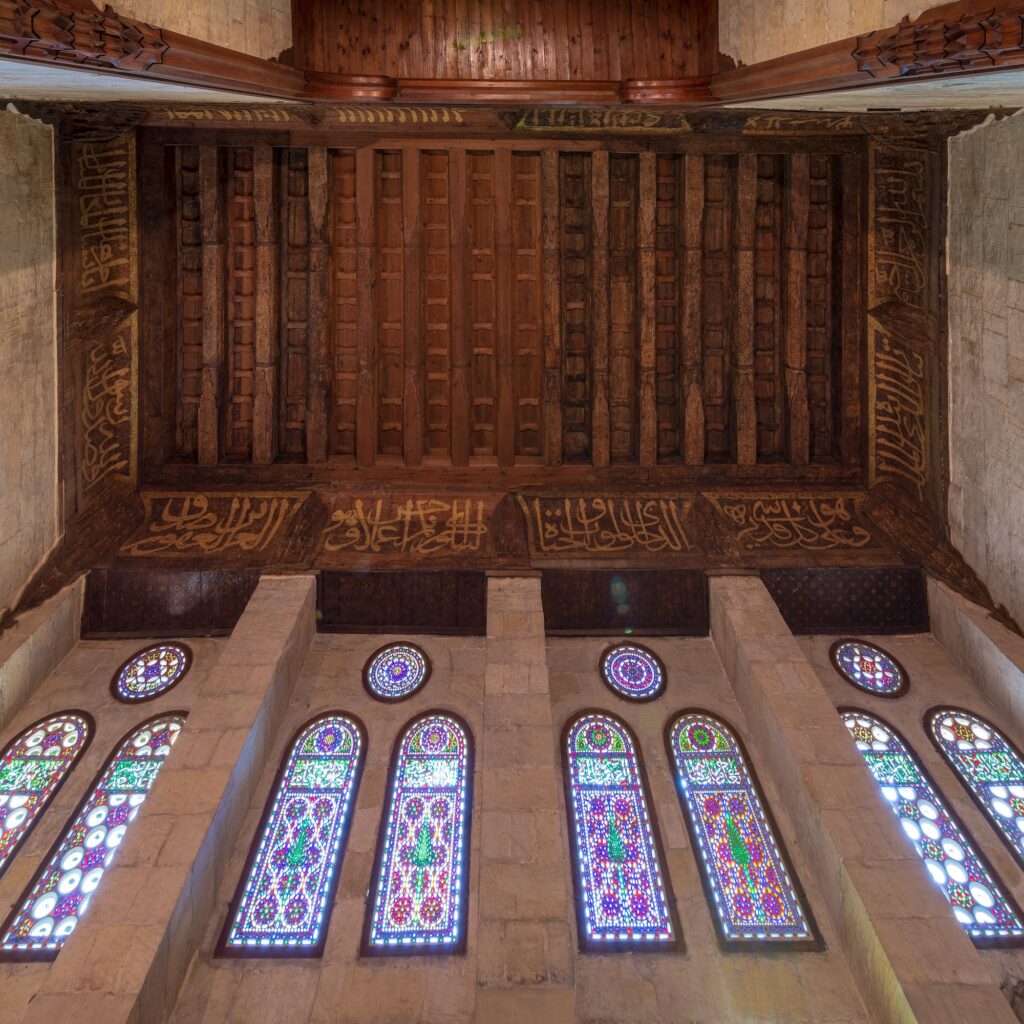 Wooden ornate ceiling with floral pattern decoration and colorful stained glass windows inside the Sultan al-Ghuri Mausoleum, Cairo
