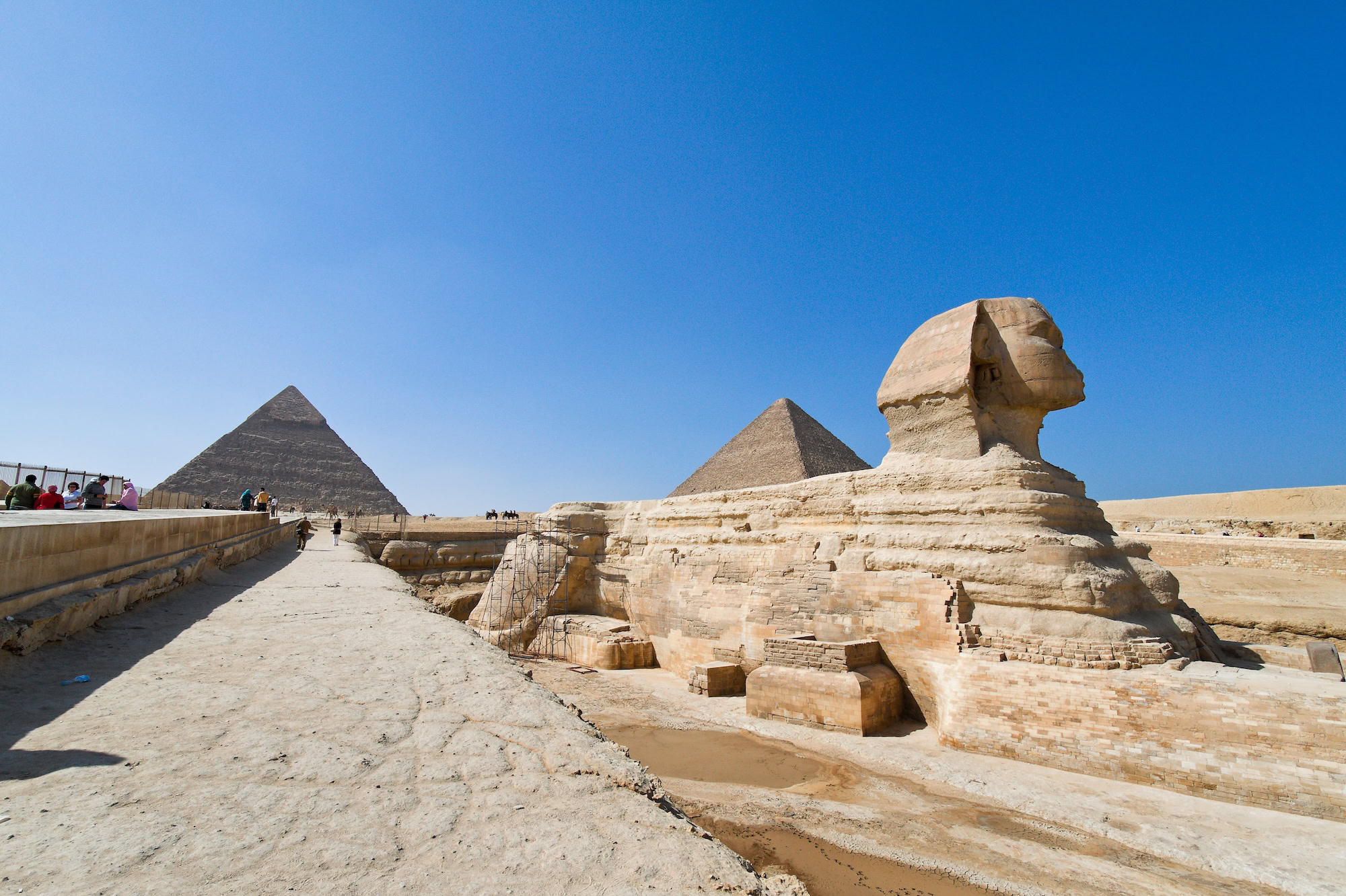 The Great Sphinx of Giza in foreground with pyramids visible in background under blue sky