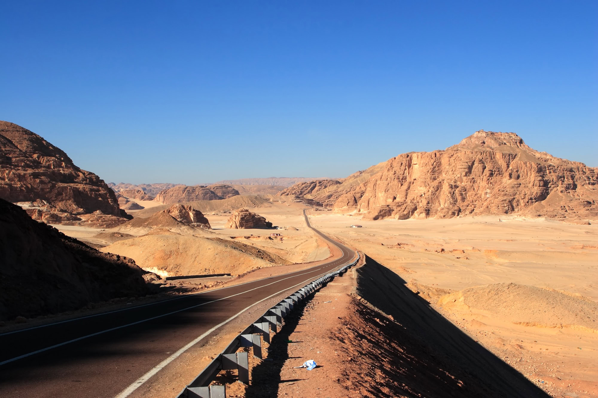 Desert highway winding through rocky landscape with mountains in background