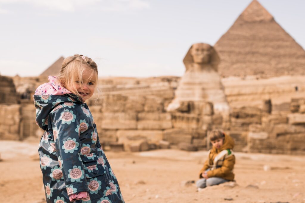 A young girl and boy standing and playing in front of the massive limestone statue on the desert plateau, Great Sphinx, Giza