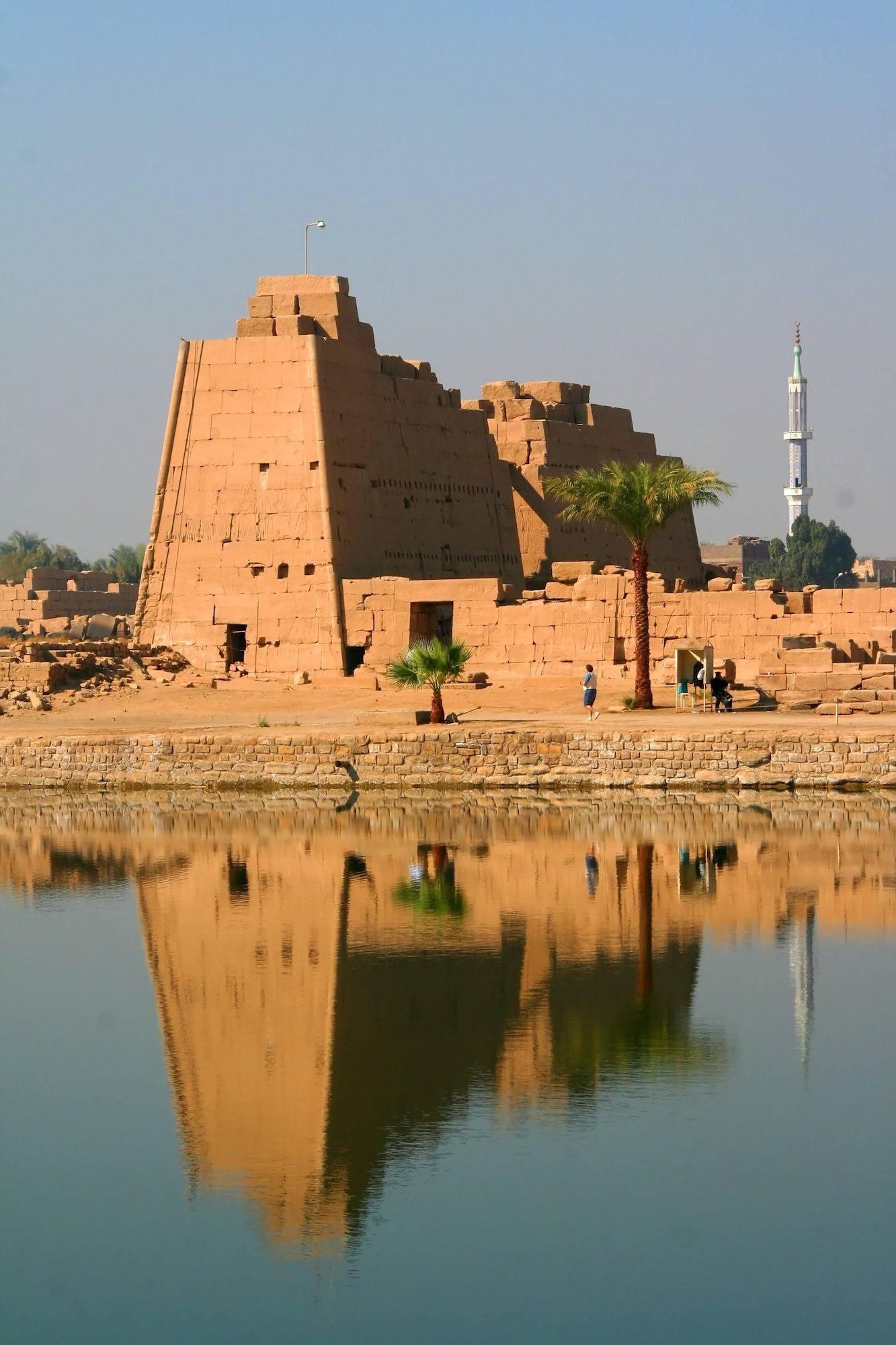 Serene view of Karnak Temple Complex with sacred lake reflecting ancient walls and palm trees