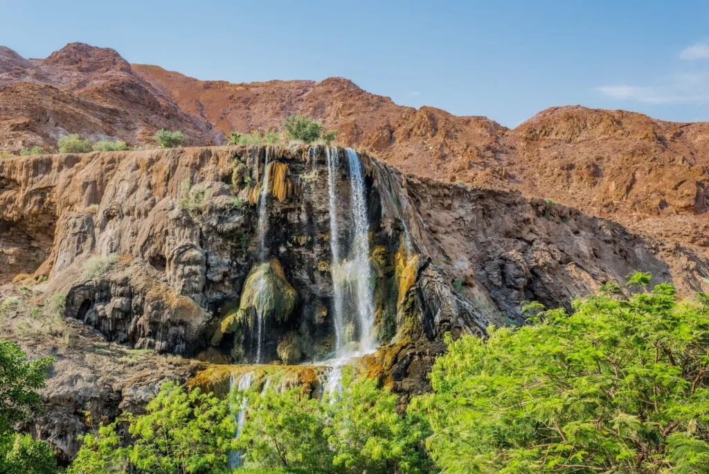 Waterfall flowing into thermal hot springs with steam rising among rocky cliffs, Ma'in Hot Springs, Madaba