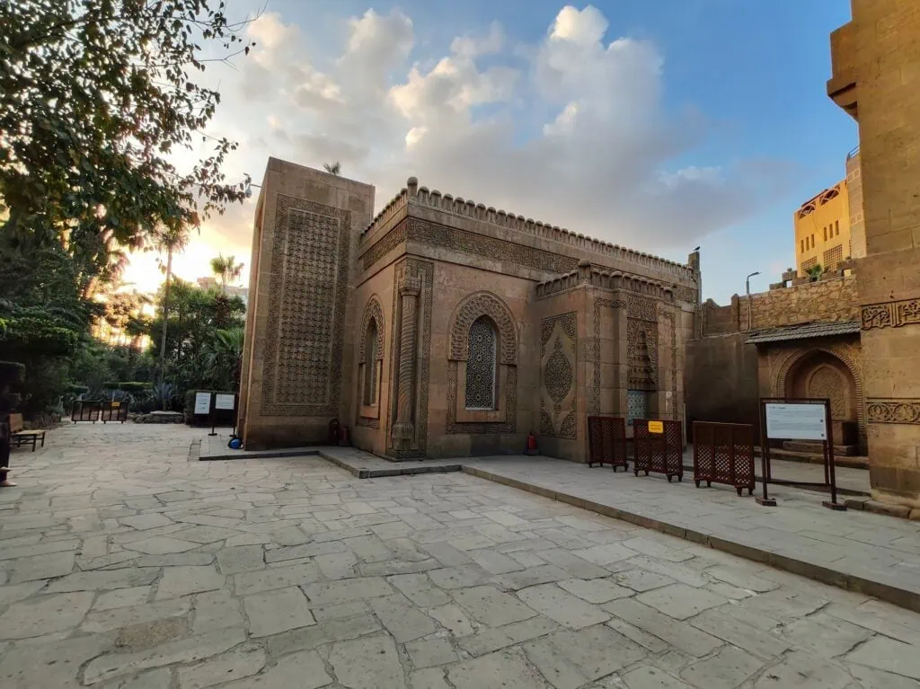 An exterior view showing carved stone walls, arched openings, and decorative architectural details of the Manial Palace mosque, Cairo