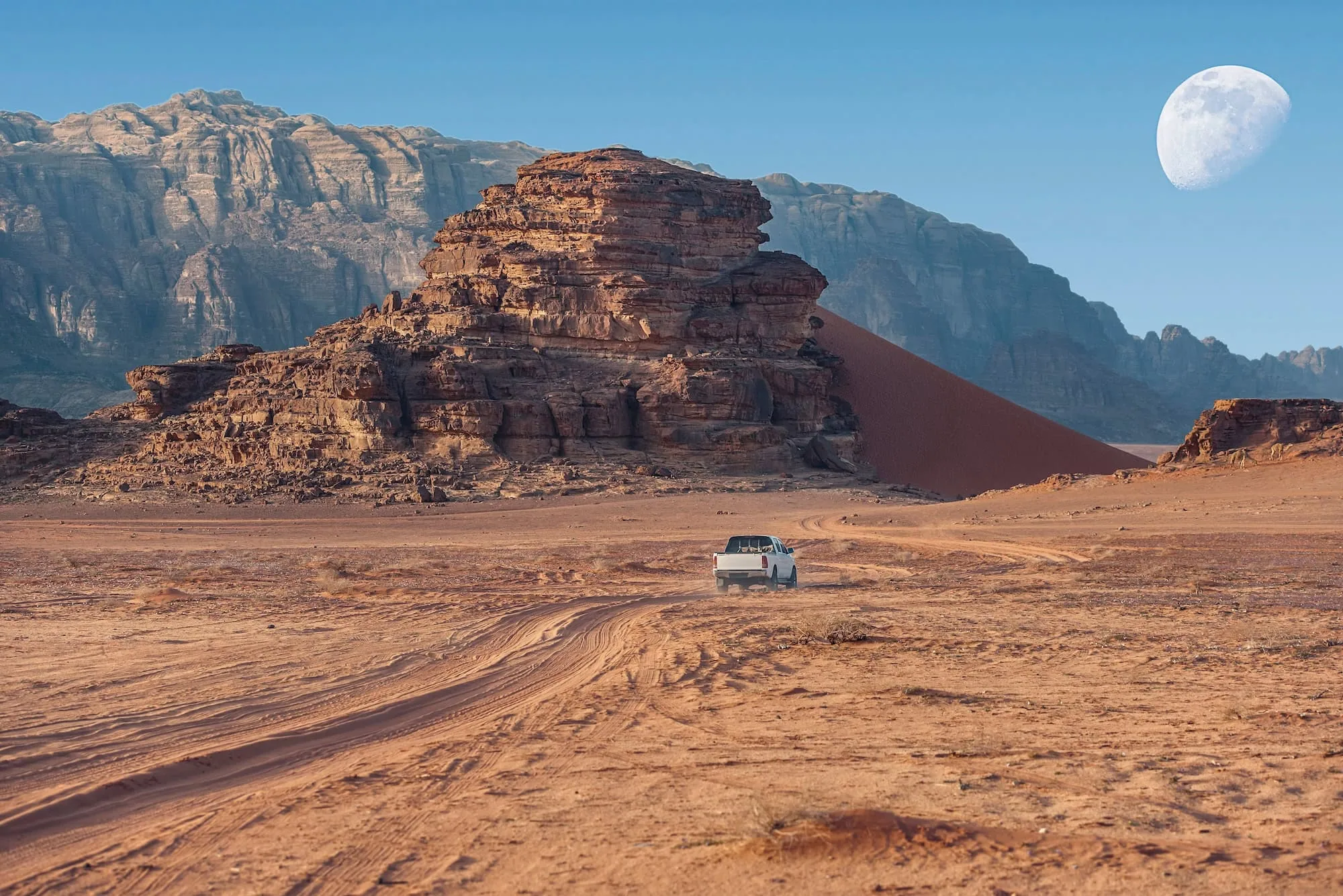 White off-road jeep driving through red desert landscape of Wadi Rum with sandstone formations and crescent moon