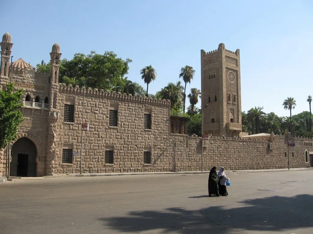 Women walking outside the exterior walls of Manial Palace with the clock tower visible in the background, Cairo