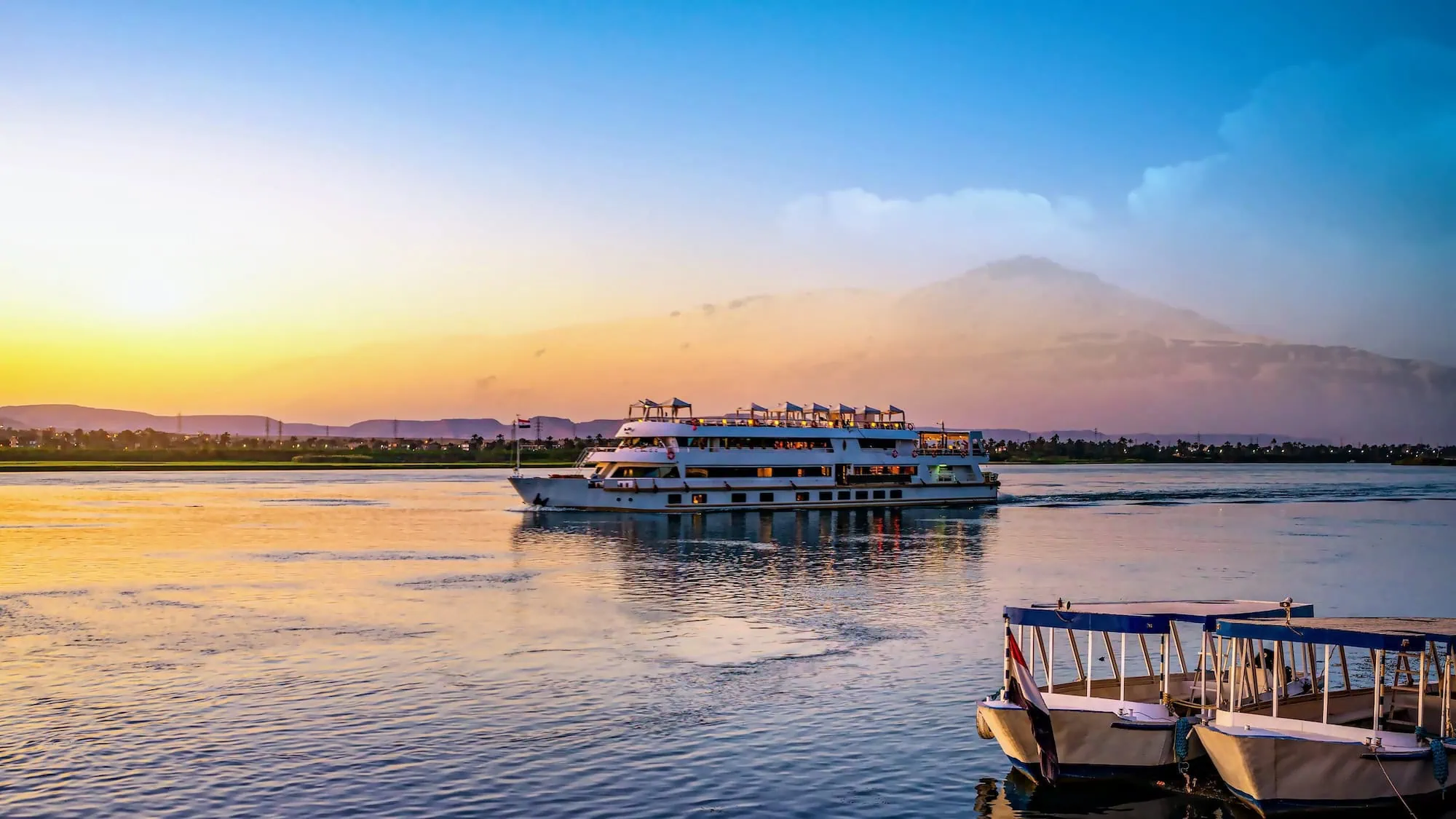 Crucero por el Río Nilo al atardecer con barcos y montañas reflejados en el agua