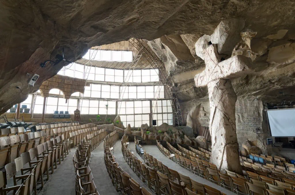A large cave hall with a prominent carved cross and rock walls inside Saint Samaan the Tanner Monastery, Cairo