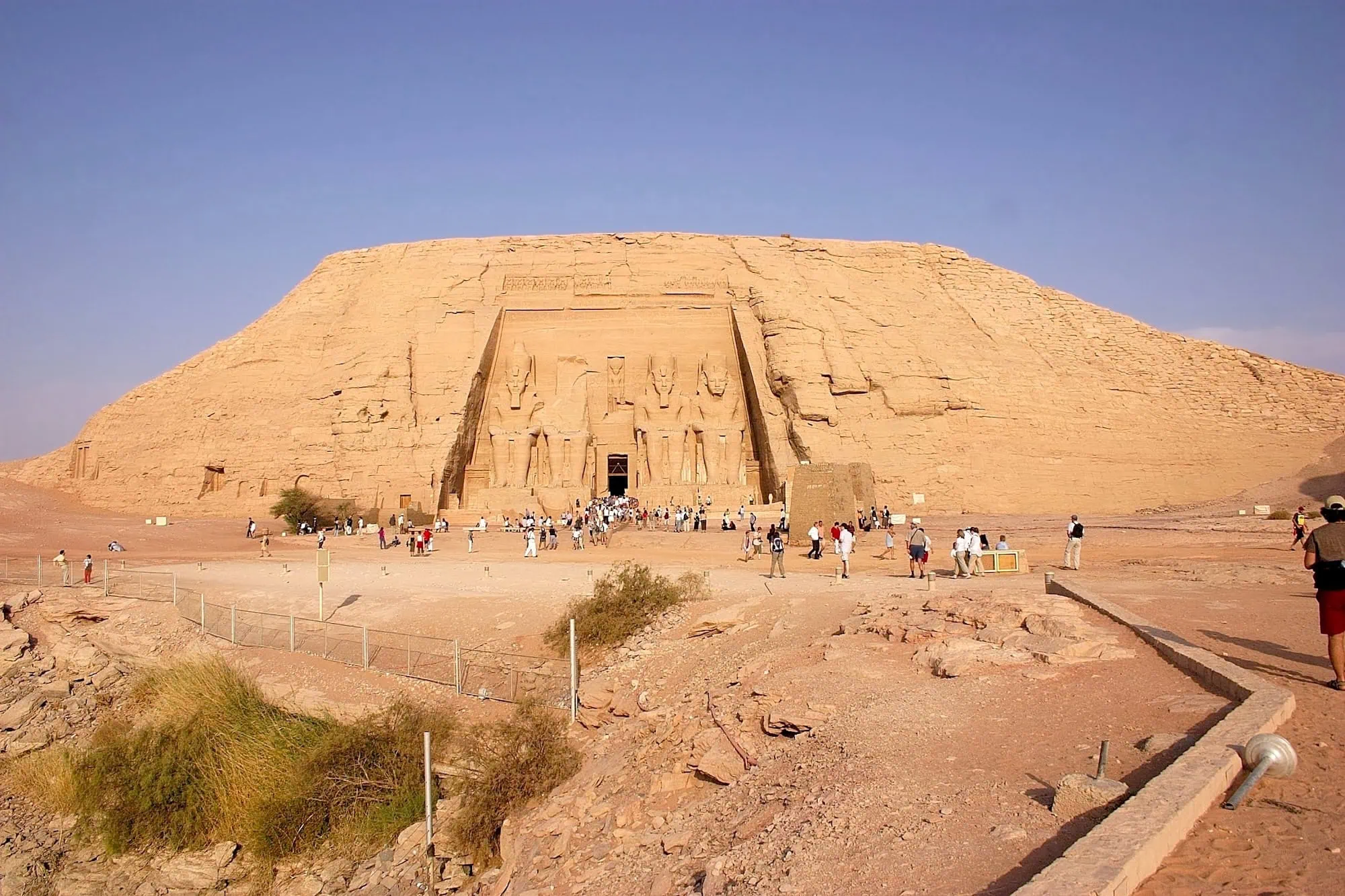 Abu Simbel temple with visitors walking on pathway near majestic pharaoh statues