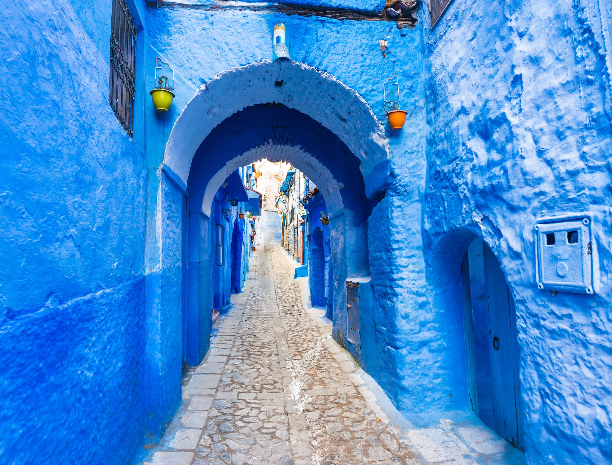 Passagem arqueada na medina azul de Chefchaouen com paredes pintadas de azul e lanternas coloridas