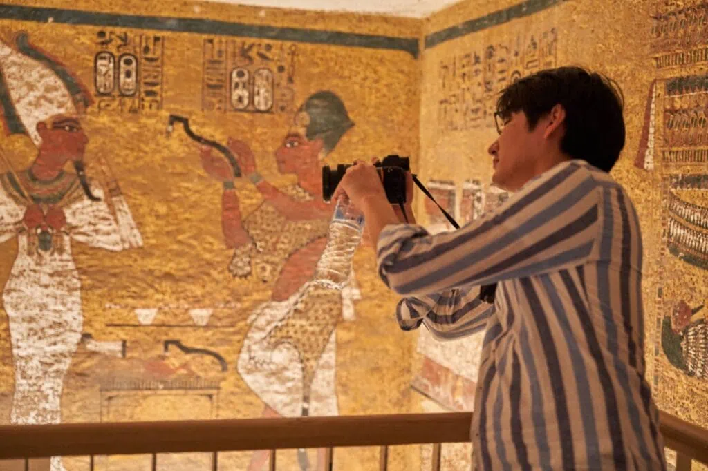 A tourist photographing sculptural wall details inside the Tomb of Pharaoh Tutankhamun in the Valley of the Kings, Luxor
