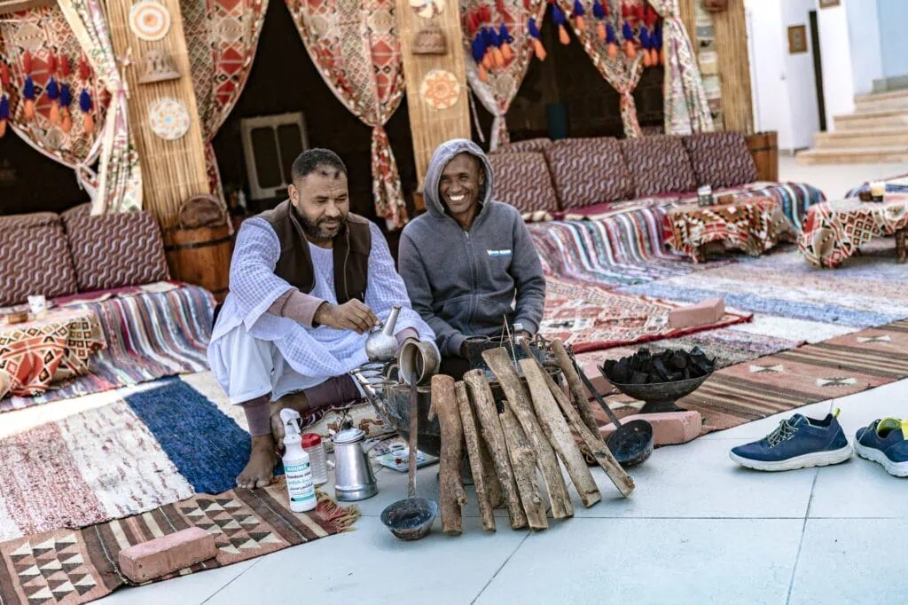 Two Bedouin men preparing and serving traditional tea inside a decorated Bedouin tent, Marsa Alam