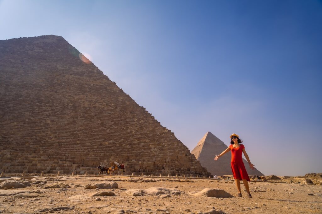 A young girl in a red dress standing near the Pyramid of Cheops with surrounding pyramids visible on the plateau, Cairo