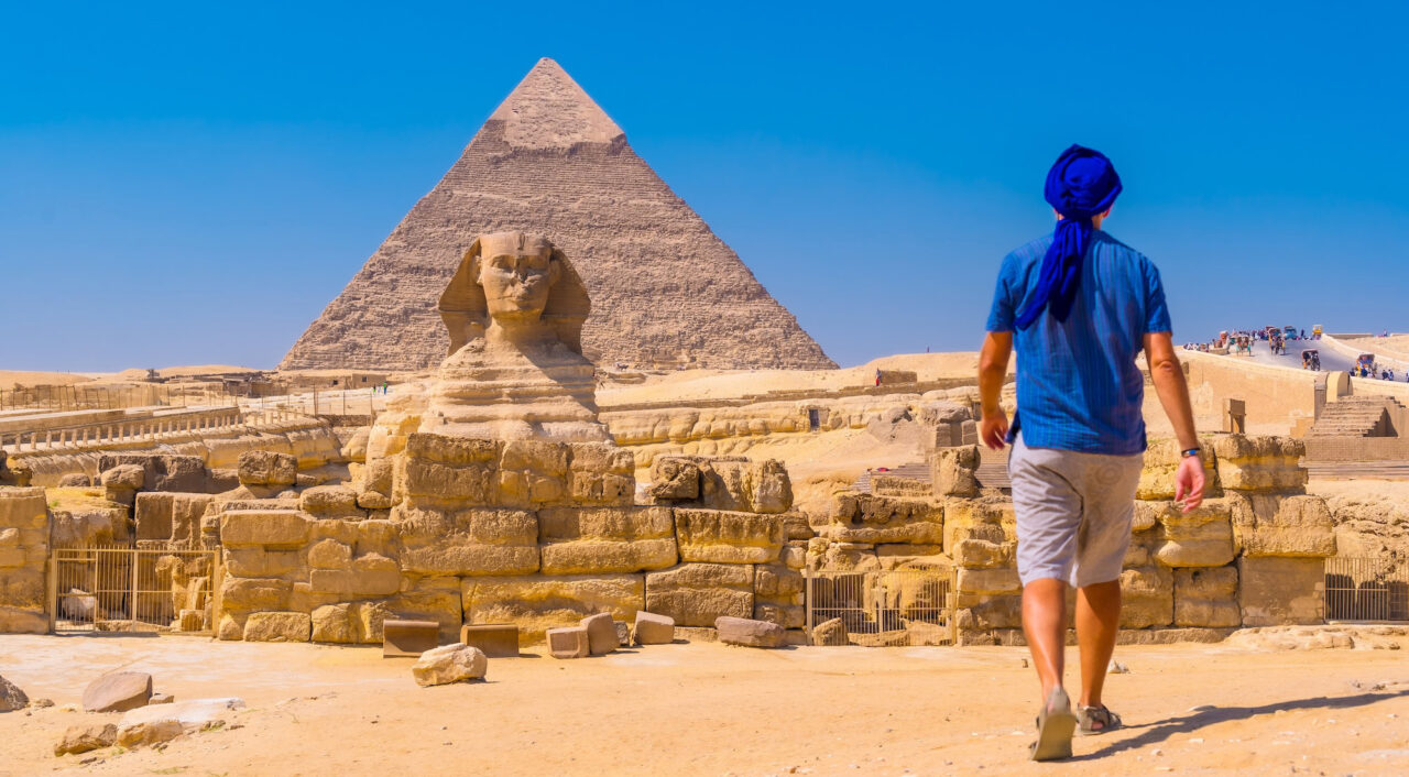 A young man walking towards the Great Sphinx of Giza and in the background the pyramid of Khafre, the pyramids of Giza