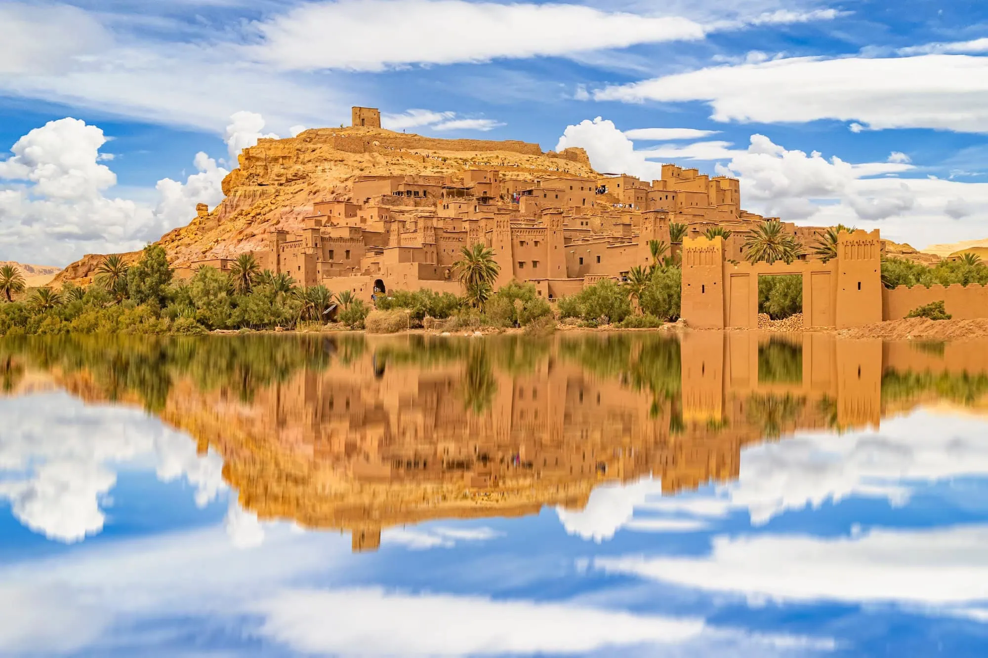 Traditional Berber village built into Atlas Mountains with mud-brick terraced buildings reflected in water