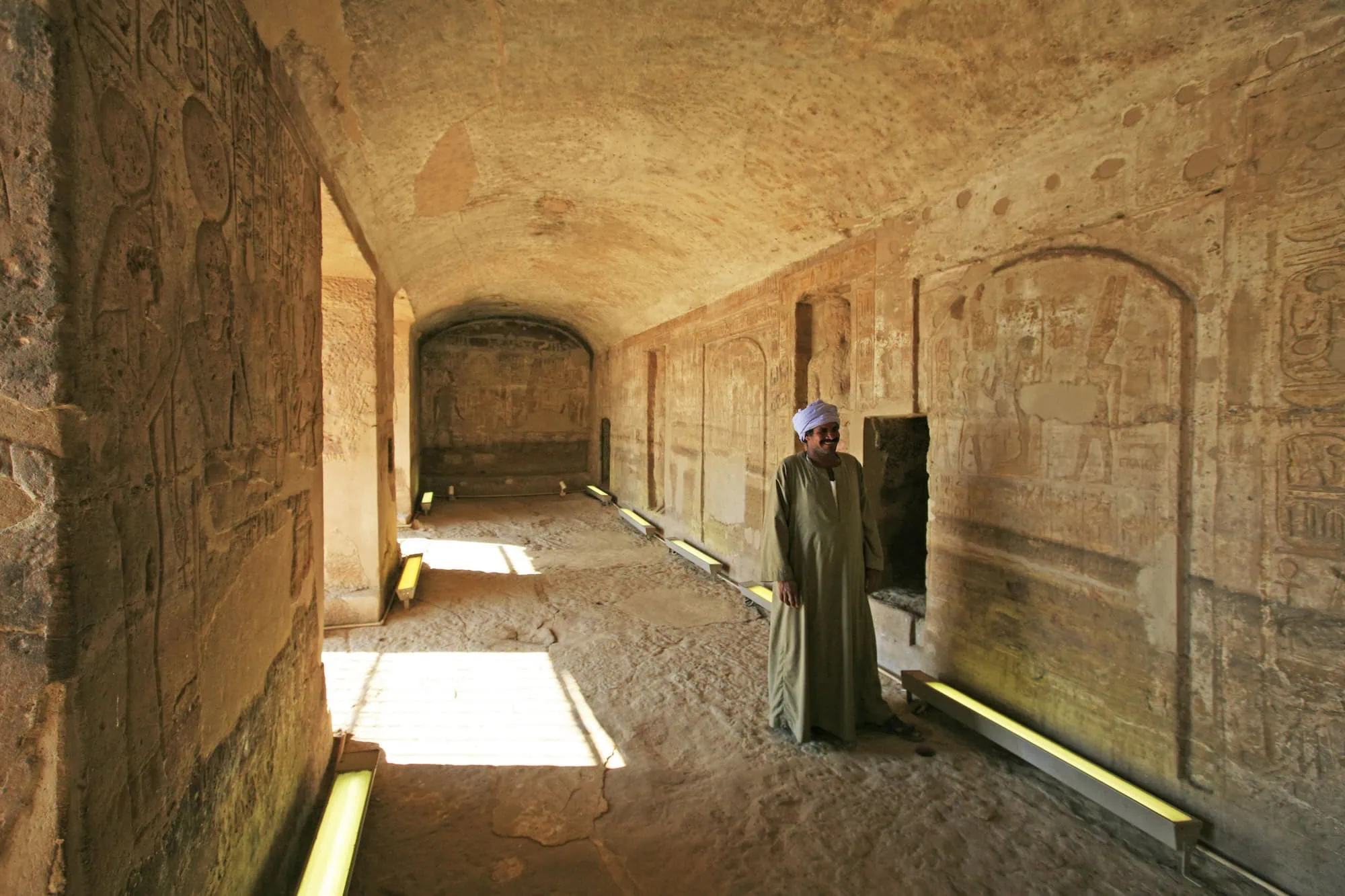 Guide in traditional dress leading premium tomb tour with ancient Egyptian hieroglyphs and stone carvings