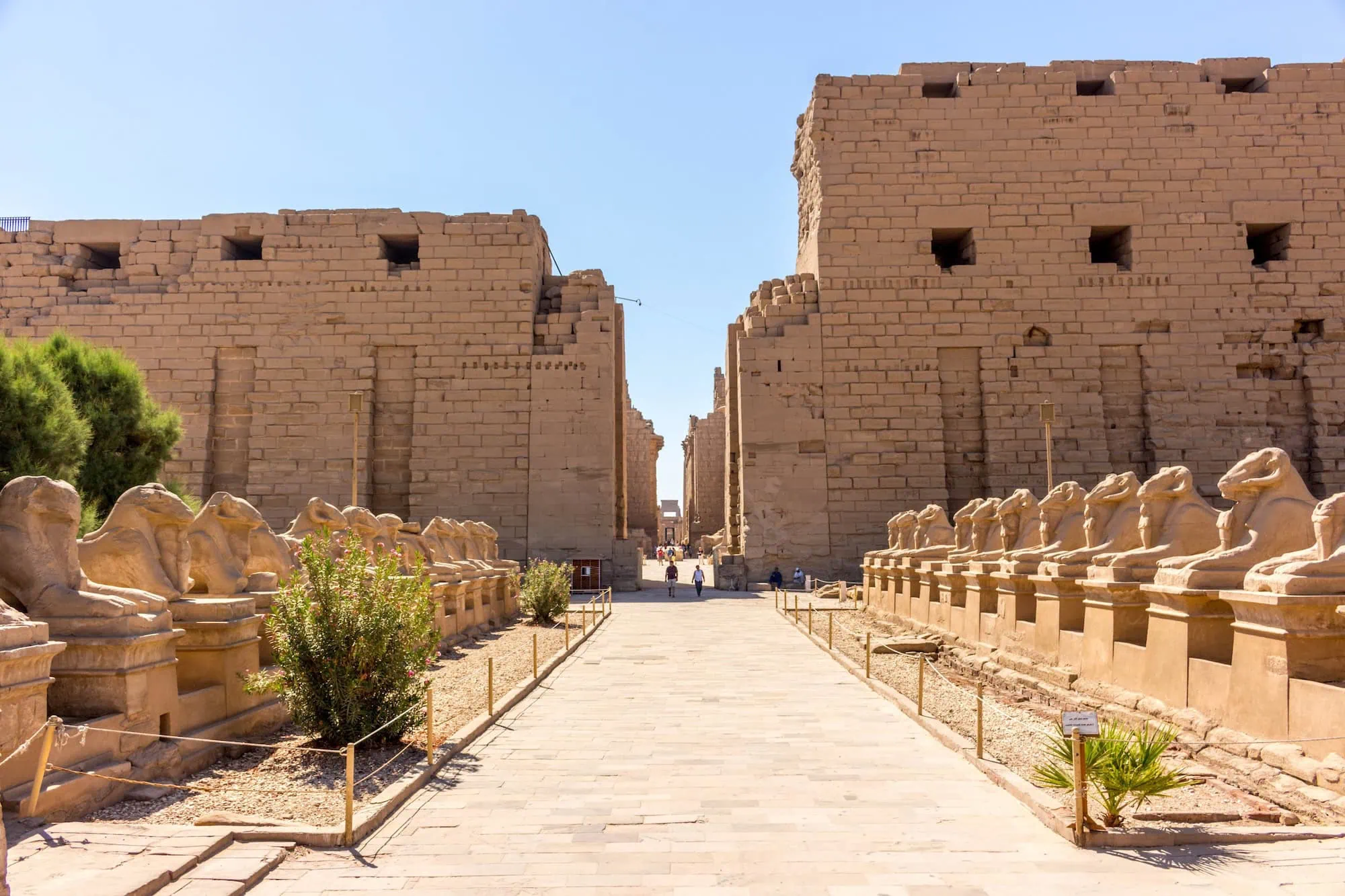 Avenue of Sphinxes at Karnak Temple with ancient sandstone walls and tourists walking through ruins