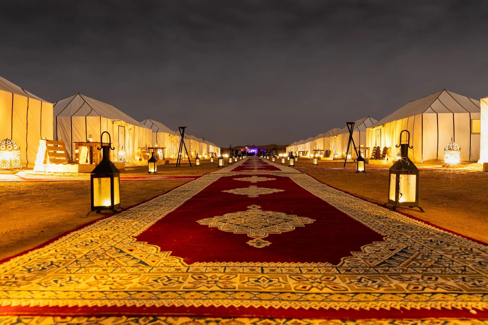 Luxury desert camp with illuminated tents and ornate carpet in Sahara Desert at night